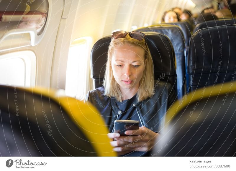 Woman using mobile phone as entertainment on airplane during commercial flight. woman look looking aircraft transport transportation travel trip sunglasses seat