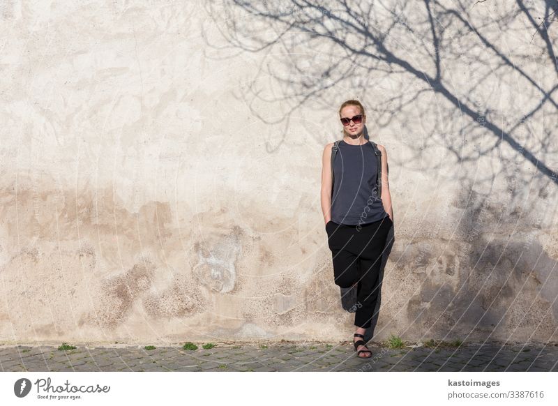 Graphical and textured artisic image of modern trendy fashionable woman wearing sunglasses leaning against old textured retro wall with tree shadow falling on the wall.