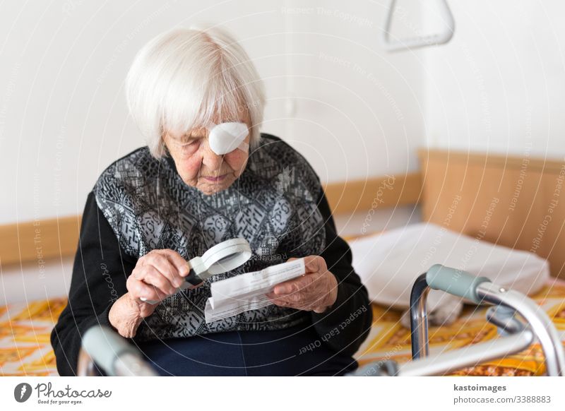 Visually impaired elderly 95 years old woman sitting at the bad trying to read with magnifying glass. senior vision eyesight visually impaired pensioner care