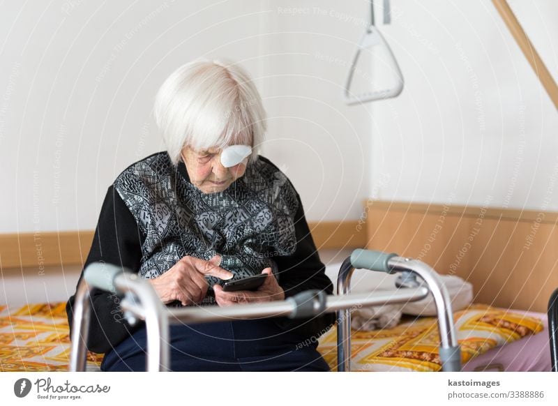 Lonley elderly 95 years old woman sitting at the bad using modern mobile phone. senior pensioner care disability hospital mobility home citizen clinic retiree