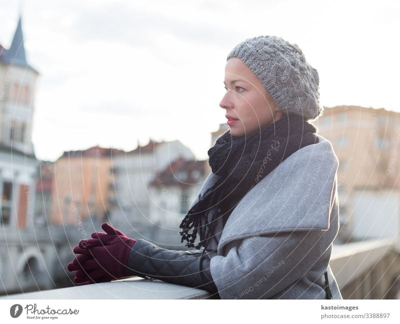 Portrait of beautiful young woman overlooking Ljubljanica river in Ljubljana, Slovenia in winter time cold lady coat gloves cap freezing city urban portrait