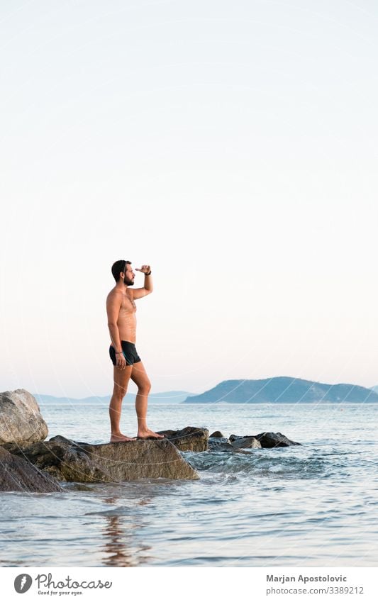 Young man standing on the rock enjoying the sunset by the sea adult alone background beach calm caucasian coast dusk evening free freedom handsome healthy