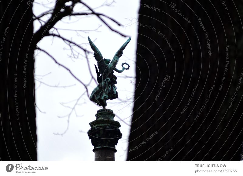 On a victory column surrounded by winterly bare trees, it seems that an angel with mighty wings and a wide dress dances on one leg and waves a victory wreath in the hand of an angled outstretched arm