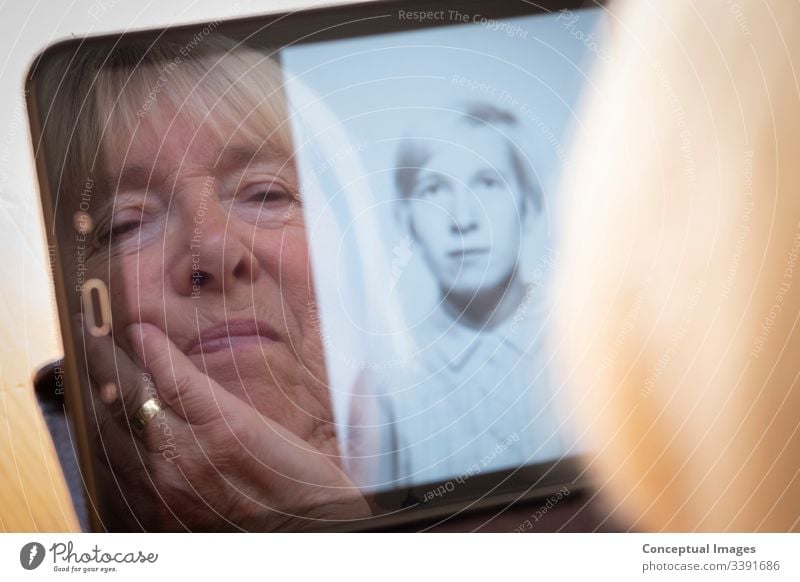 Senior caucasian woman looking at old photos of herself as a young woman on a tablet computer photography themes memories the ageing process contrasts