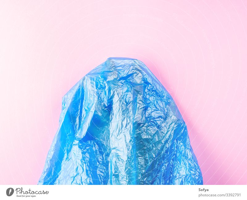 Human hand trapped in plastic bag on pink background. Conceptual flat lay ocean pollution metaphor sea water blue symbol nature plastic free stop help concept