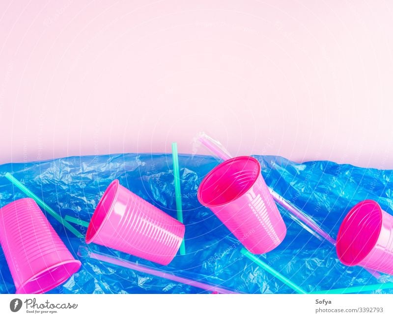 Plastic straws and cups in ocean represented by blue plastic bag. Pollution concept. Flat lay on pink glass disposable floating pollution sea metaphor throw