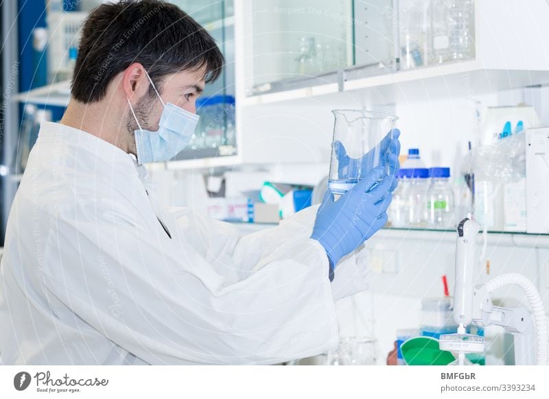 man in laboratory holding a glass an watching the liquid in it analysis analyzing biological biotechnology care chemical chemist chemistry clinic corona