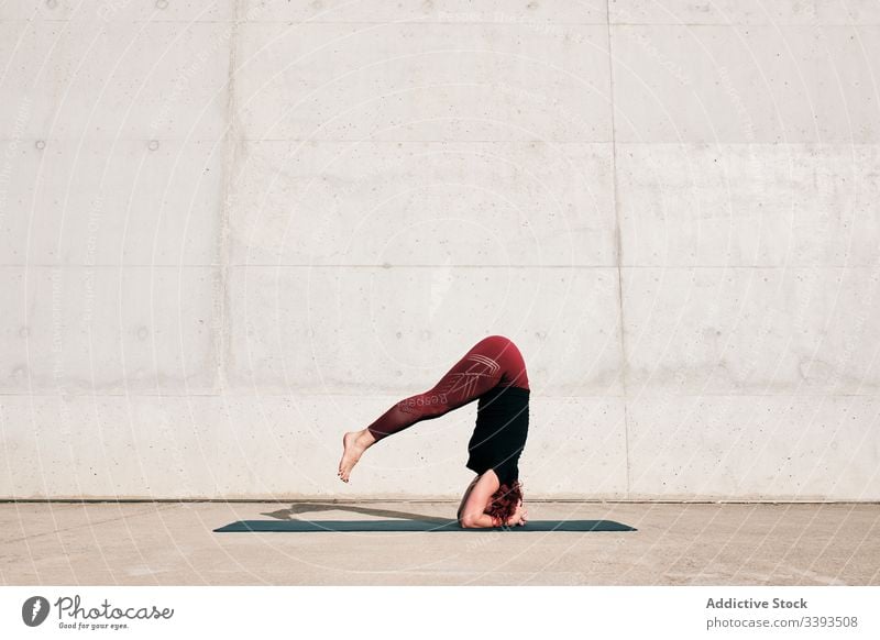 Woman doing balance exercise in headstand pose while practicing yoga on street woman acrobatic practice training urban sirsasana concrete strong flexible