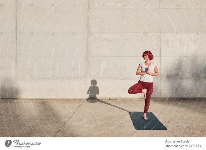 Woman doing balance exercise in tree pose while practicing yoga on street athlete namaste woman meditate practice training stretch barefoot concrete calm