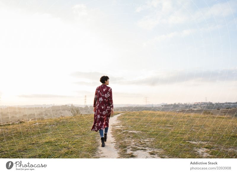 Anonymous female hipster in trendy outfit on empty rural road woman casual nature teen suburb field countryside grass sky lifestyle young cloudy walk meadow