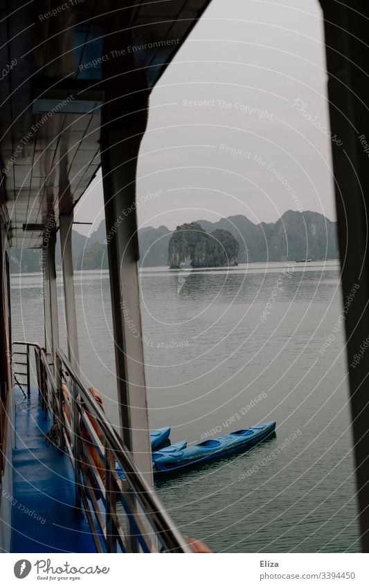 View from an excursion boat, with railing and tethered kayaks, in Halong Bay in Vietnam; beautiful landscape with limestone cliffs rising out of the sea, in foggy weather