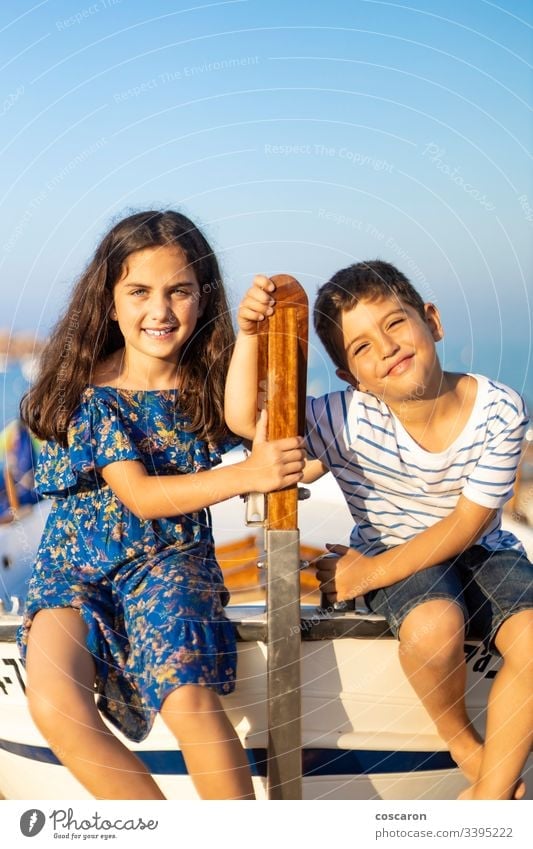 Portrait of two young children climbed in a fishing boat on the beach adventure blue board boy brothers captain childhood coast coastal cruise dress family