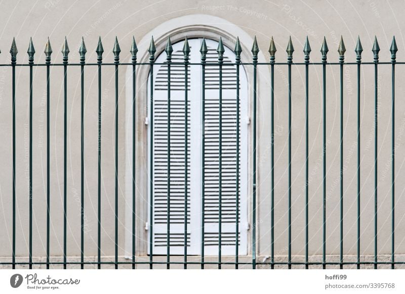elegant high fence in front of windows with closed shutters Fence Arrow Window Shutter Lattice window Quarrystone facade Facade Wall (barrier) Wall (building)