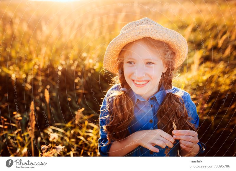 happy kid girl in blue dress and straw walking on summer sunny meadow. Lifestyle shot, rural living and summer traveling concept child nature lifestyle