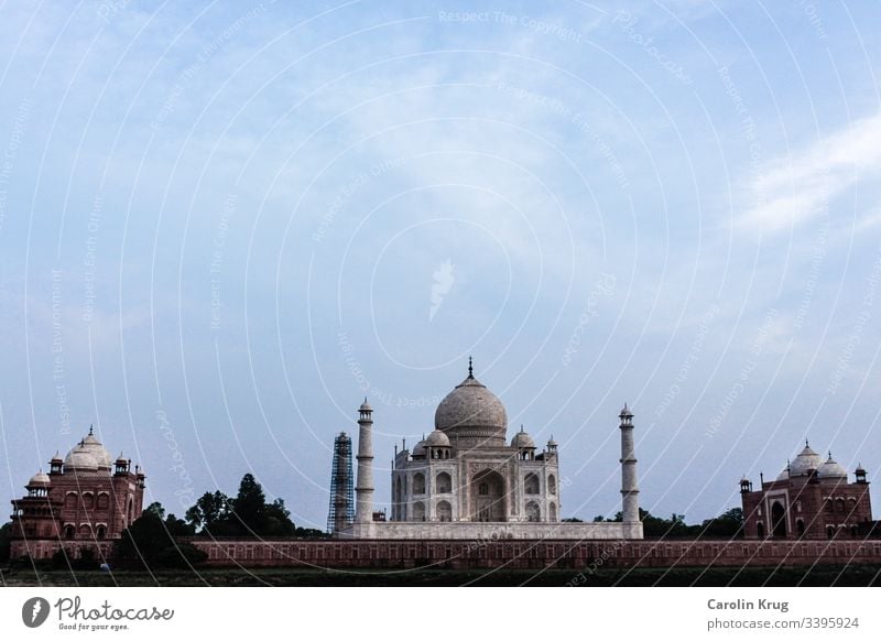 The fairytale Taj Mahal with its two outbuildings. Almost as if the two outbuildings made of sandstone guard the wonderful queen, the tomb of a great love.  A long shot from the other side of the holy Yamuna River