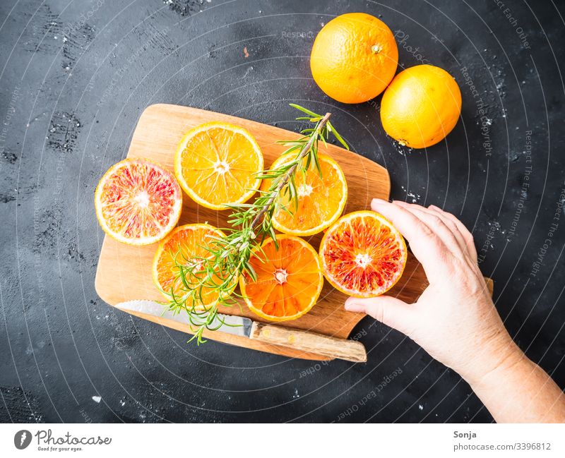 Hand mit frischen halbierten Orangen auf einem Holzschneidebrett auf einem schwarzen Hintergrund hand frau orange holz messer rustikal draufsicht Fruit Arm