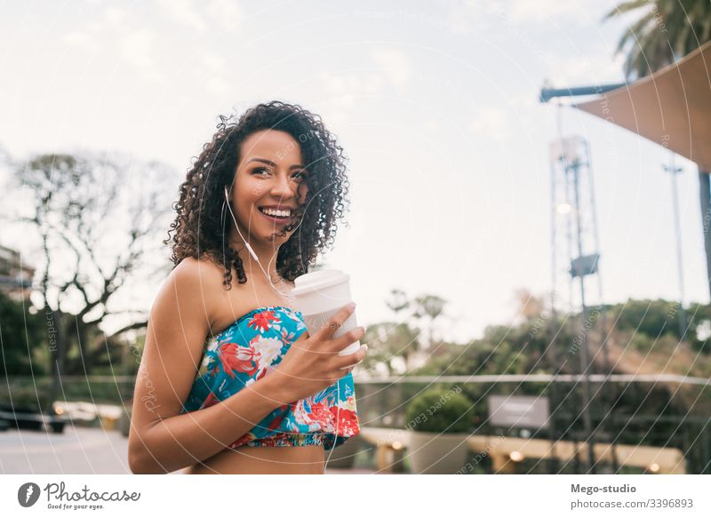 Afro woman listening to music while holding a cup of coffee. coffee cup earphones female afro street ethnicity outside stylish beauty positive relaxing outdoors