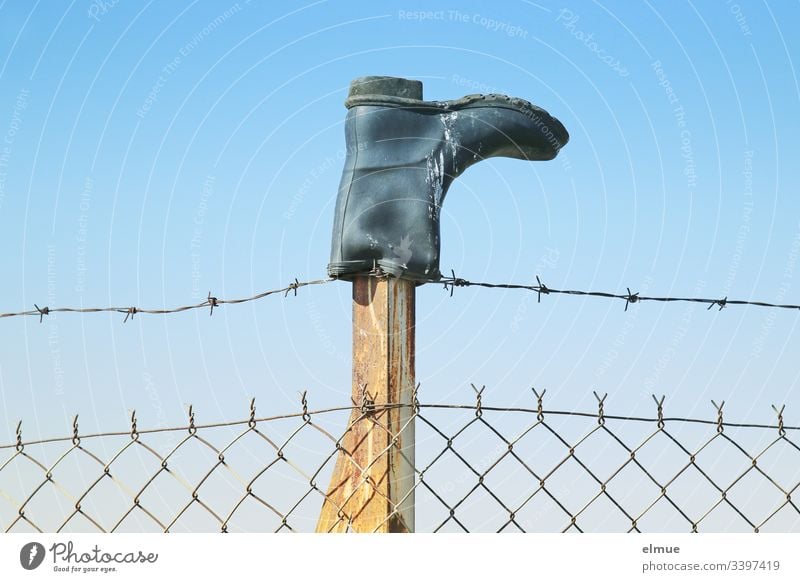 Gumboots on a fence post Rubber boots Boots Fence Barbed wire Sky Bird droppings Inverted Border Blue Protection Barbed wire fence Wire netting fence Deserted