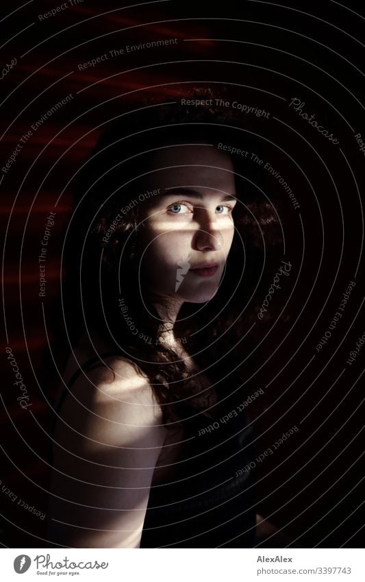 Portrait of a young woman in light stripes of blinds in front of red wall -  a Royalty Free Stock Photo from Photocase