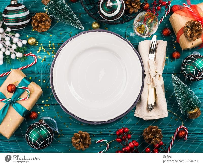 Christmas dark background with empty dish on emerald green wooden table full of festive ornament, gift boxes and candy canes christmas new year dinner holiday
