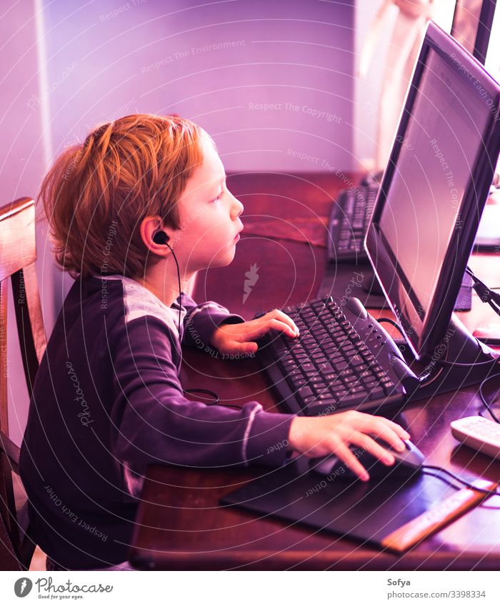 Cute little boy playing at pc concentrated. Purple tone computer child kid technology internet leisure male person lifestyle music modern home caucasian game