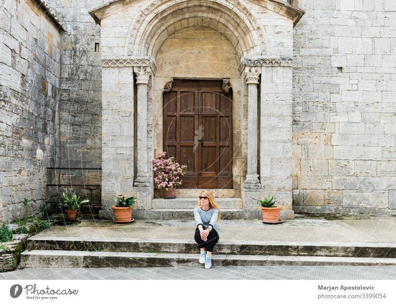 Young female traveler sitting on steps of medieval church in Tuscany, Italy adult ancient antique architecture building casual catholic culture door enjoying