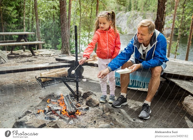 Man and woman making coffee in big kettle on campfire in forest on shore of  lake, making a fire, grilling. Happy couple exploring Finland. Scandinavian  landscape. - a Royalty Free Stock Photo