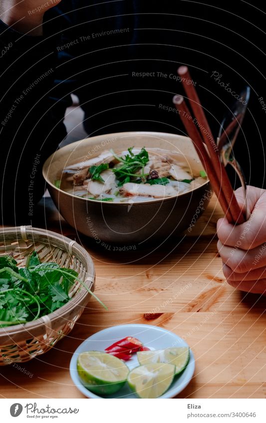 A bowl of Vietnamese Pho soup with fresh herbs and a person with chopsticks in his hand while eating Soup Pho Bo Fresh salubriously vacation Eating Hot limes