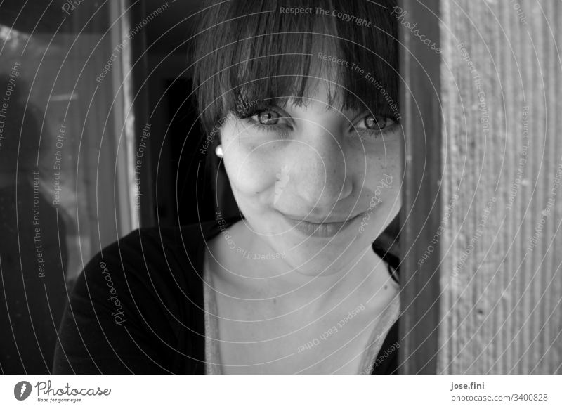 Young woman with bangs, looks into the camera and smiles fringe hairstyle Smiling kind Open Looking Black & white photo Looking into the camera pretty Feminine
