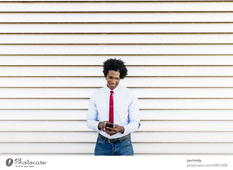 Black Businessman using a smartphone with a white blinds background black businessman curly afro you hair suit african male adult portrait american person