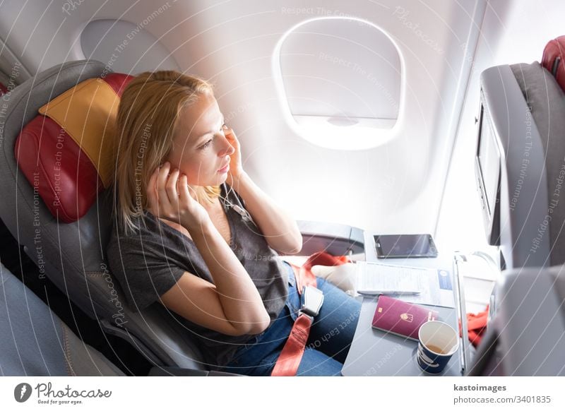 Woman flying on commercial passengers airplane, listening to music. flight travel woman young aircraft female cabin caucasian entertainment headphones cup