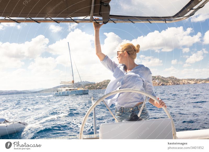 Attractive blond female skipper navigating the fancy catamaran sailboat on sunny summer day on calm blue sea water. nautical steering wheel sailing boat woman