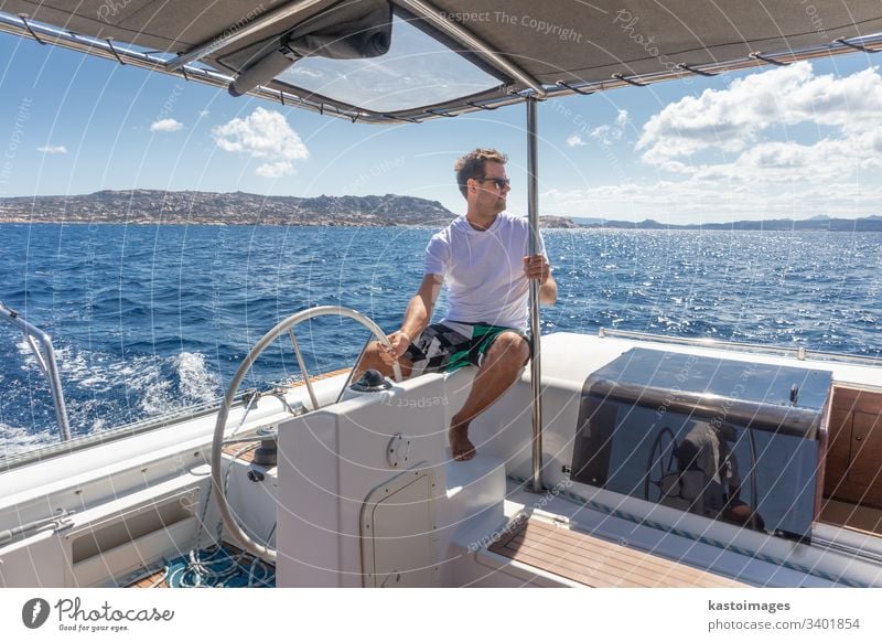 Attractive male skipper navigating the fancy catamaran sailboat on sunny summer day on calm blue sea water. nautical steering wheel sailing boat ocean ship