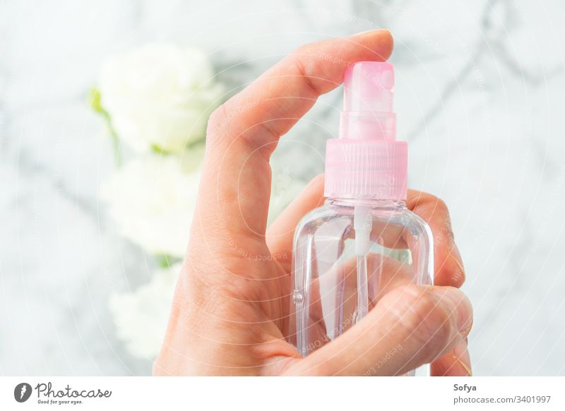 Woman's hand spritzing liquid from spray over marble background with white flowers bottle small pink hair product beauty care cosmetics tonic face push use