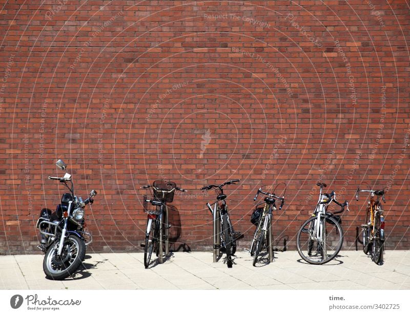 Parking space management ::: five bicycles and a power bolt basking in the sun on a boring red brick wall Brick wall Bicycle Parking lot Motorcycle sunny