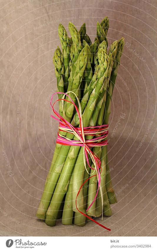 Green asparagus in bunch, held with a colourful ribbon with style, in front of a brown wall at the healthy asparagus season in spring. Asparagus green asparagus