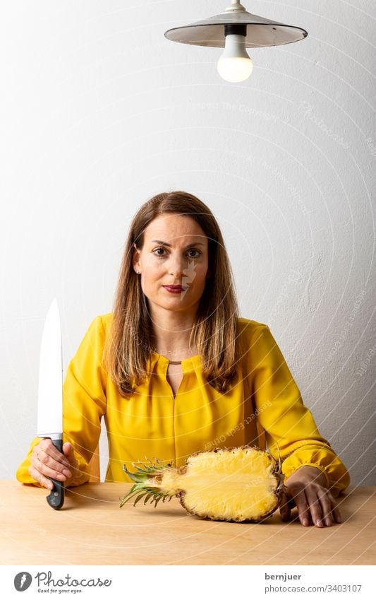Woman with knife at the table Brunette House (Residential Structure) inboard Cook chef's knife interior Kitchen half Pineapple boil Sit Lamp Blouse Yellow