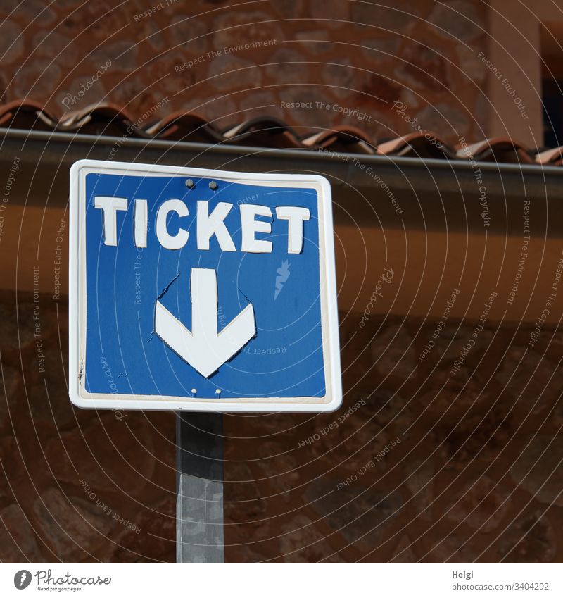 Ticket, sign with arrow pointing down in front of a wall Signage Signs and labeling Exterior shot Transport Blue White Wall (building) Brown Deserted square