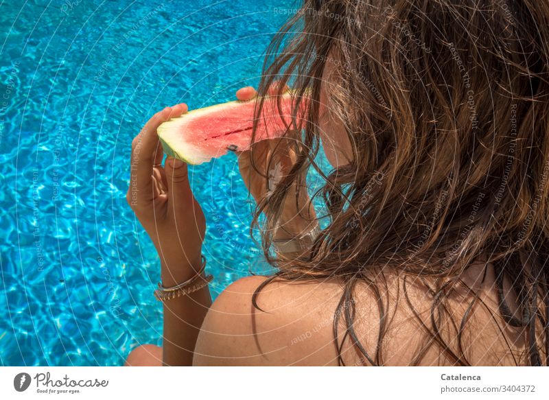 The brown-haired young woman holds a slice of watermelon in her hands while looking at the blue water Young woman Water melon Eating pool Fruit Summer Healthy