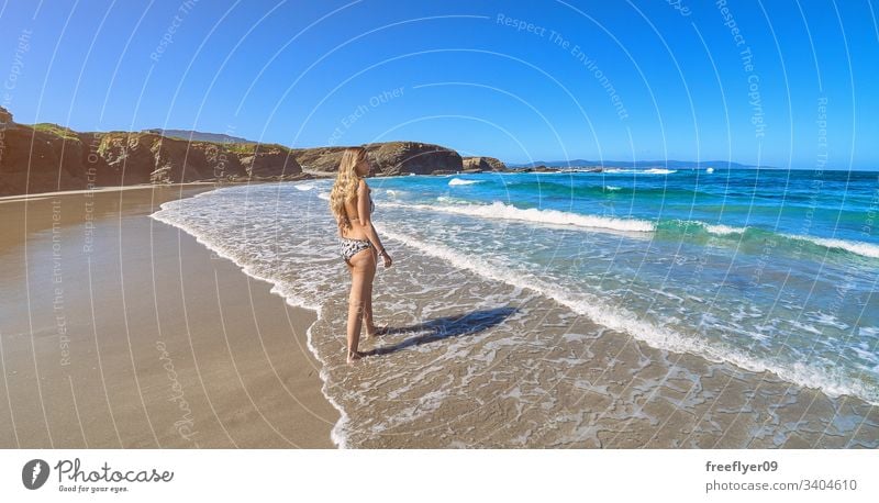 Young woman entering the ocean in a beach with cliffs in Galicia tourism hiking galicia spain ribadeo castros illas rock atlantic bay touristic cathedrals