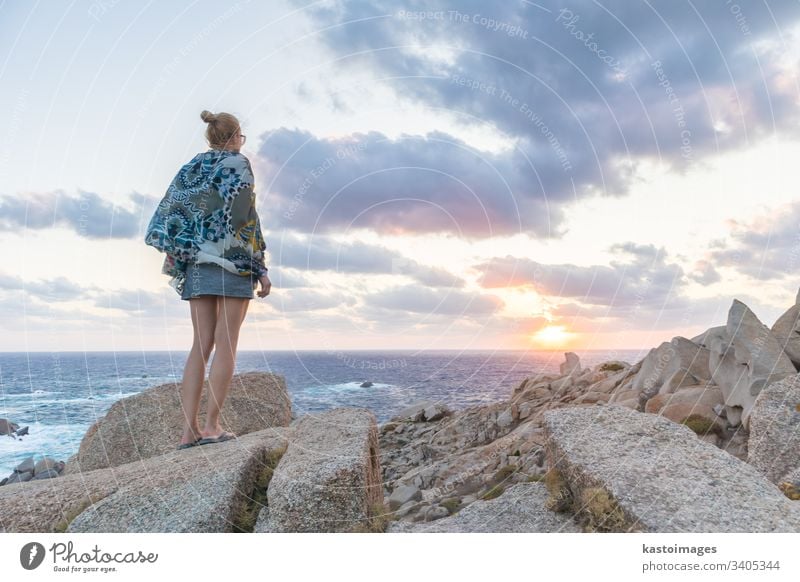 Solo young female traveler watches a beautiful sunset on spectacular rocks of Capo Testa, Sardinia, Italy. adventure lifestyle woman beach freedom landscape
