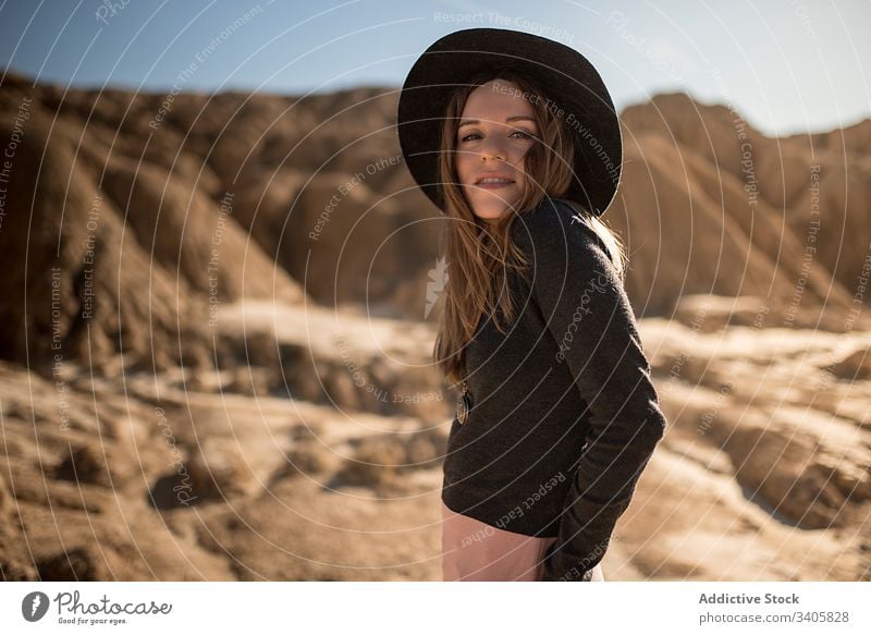 Trendy woman in dry desert style stone terrain hand in pocket countryside adjust hair bardenas reales navarre spain female eyes closed adventure nature hat