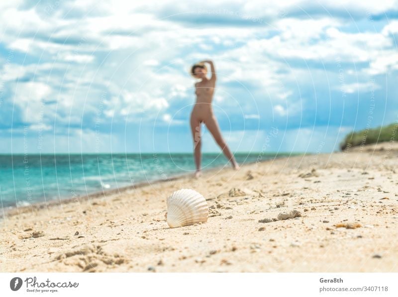 young nude girl with a hat walks on an empty beach near the sea surf against the blue sky with clouds in summer alone blur body climate day erotic female figure