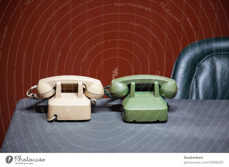 Two old telephones in beige and lime green on a desk with leather armchair in front of oxblood red wall paneling Telephone Receiver Desk Armchair back Leather