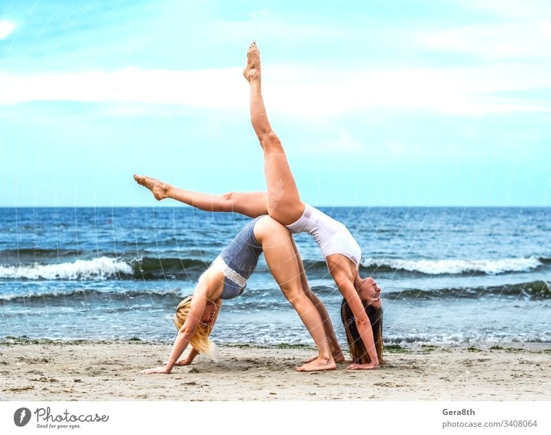 two young girls in white top and black bottom on the sandy shore acrobatic acrobatic yoga active asana beach blond blue body brown-haired calm coast