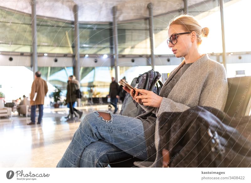 Female traveler using her cell phone while waiting to board a plane at departure gates at airport terminal. female woman business flight baggage luggage young