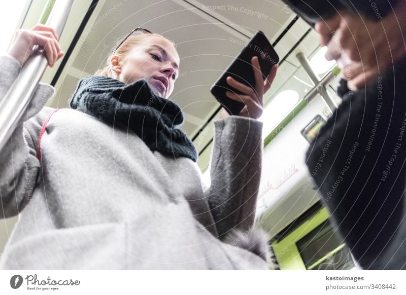 Beautiful blonde woman wearing winter coat and scarf reading on the phone while traveling by metro public transport. subway city passenger female urban train