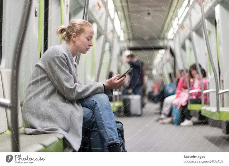 Beautiful blonde woman wearing winter coat reading on the phone while traveling by metro public transport. subway city passenger female urban train sitting