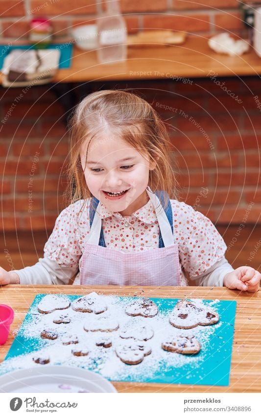 Little girl happy because of her baked cookies. Decorating cookies with colorful sprinkle and icing sugar. Kid taking part in baking workshop. Baking classes for children, aspiring little chefs. Learning to cook. Combining and stirring prepared ingredients