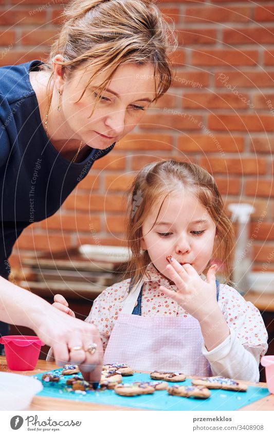 Little girl with her mom's help decorating baked cookies with colorful sprinkle and icing sugar. Kid taking part in baking workshop. Baking classes for children, aspiring little chefs. Learning to cook. Combining and stirring prepared ingredients